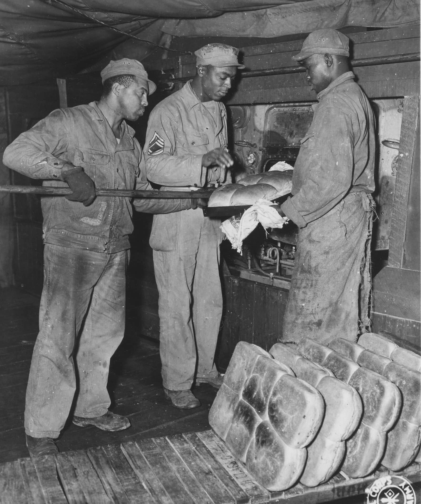 Three bakers pulling a pan of loaves from the oven
